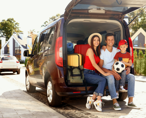 Family seated in the back of a red mini van, child is holding a soccer ball. They are choosing the perfect family car